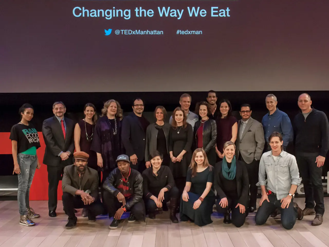 In this image we can see people on the stage and behind them, we can see a screen with some text.