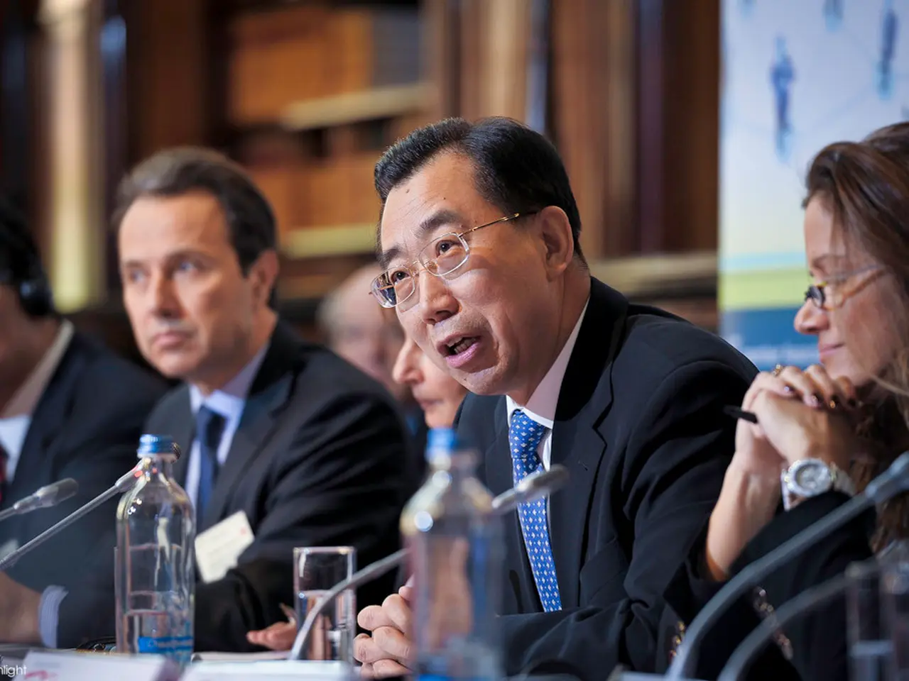 As we can see in the image, there are few people sitting and the man who is sitting here is talking...