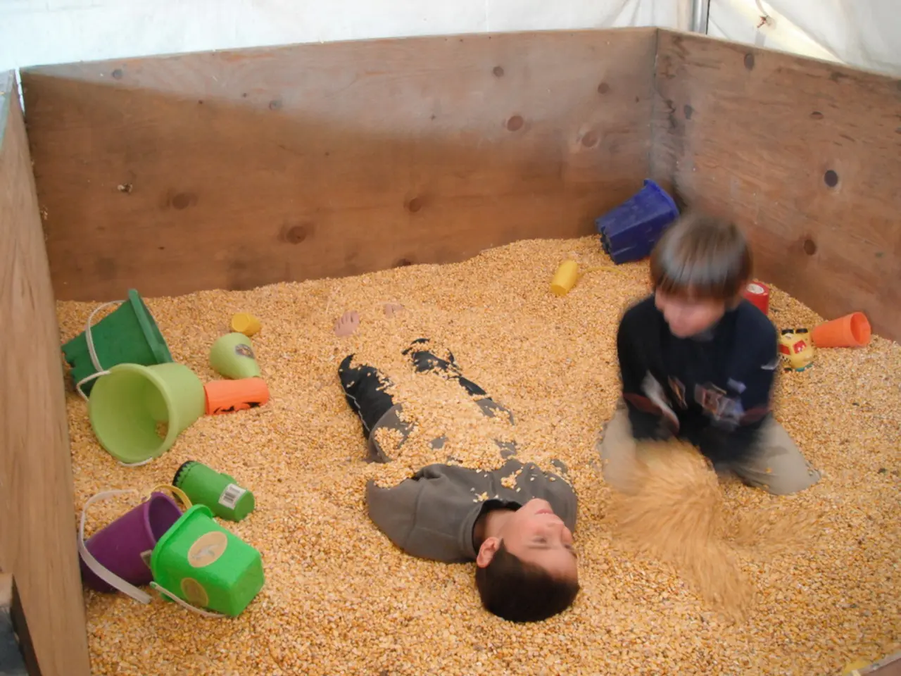 In this image, we can see a box contains sand, buckets, glasses and kids.