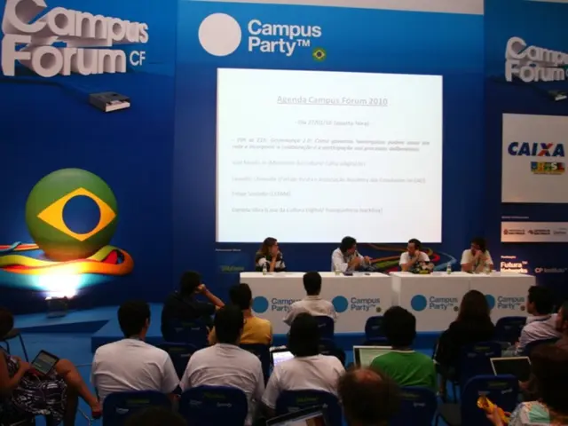 This picture is clicked in the conference hall. At the bottom of the picture, we see people sitting...