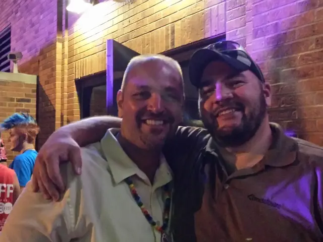 In this image we can see a group of people standing. In the background, we can see some buildings...