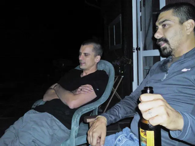 in the picture there are two persons sitting on the chair on one person is catching a bottle with...