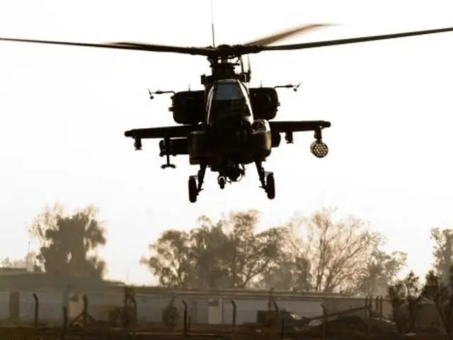 In the center of the picture there is a helicopter flying. In the background there are trees,...